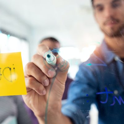 Successful young man writing on office glass board during the meeting with colleagues