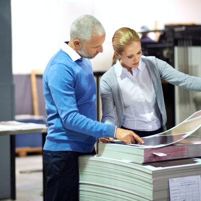 Two publishers assessing the quality of printed work in a factory